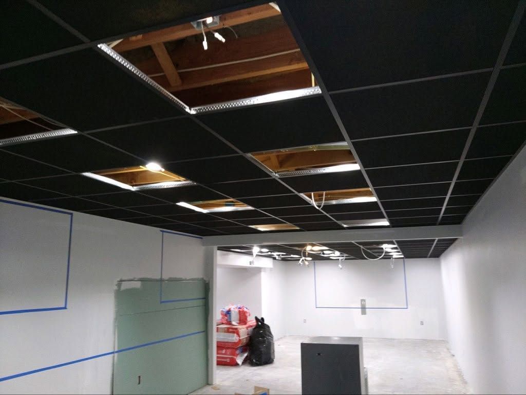 Empty office space with damaged drop ceiling tiles and scattered debris on the floor.