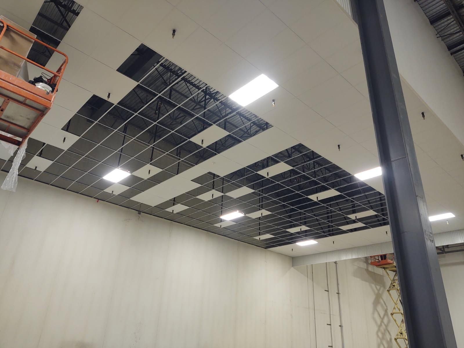Partially installed office ceiling with exposed grid, missing tiles, and bright overhead lights