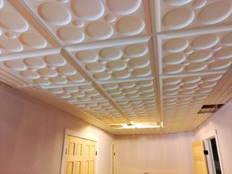 Interior room with white patterned ceiling, beige walls, and a ceiling fan above a door and window.