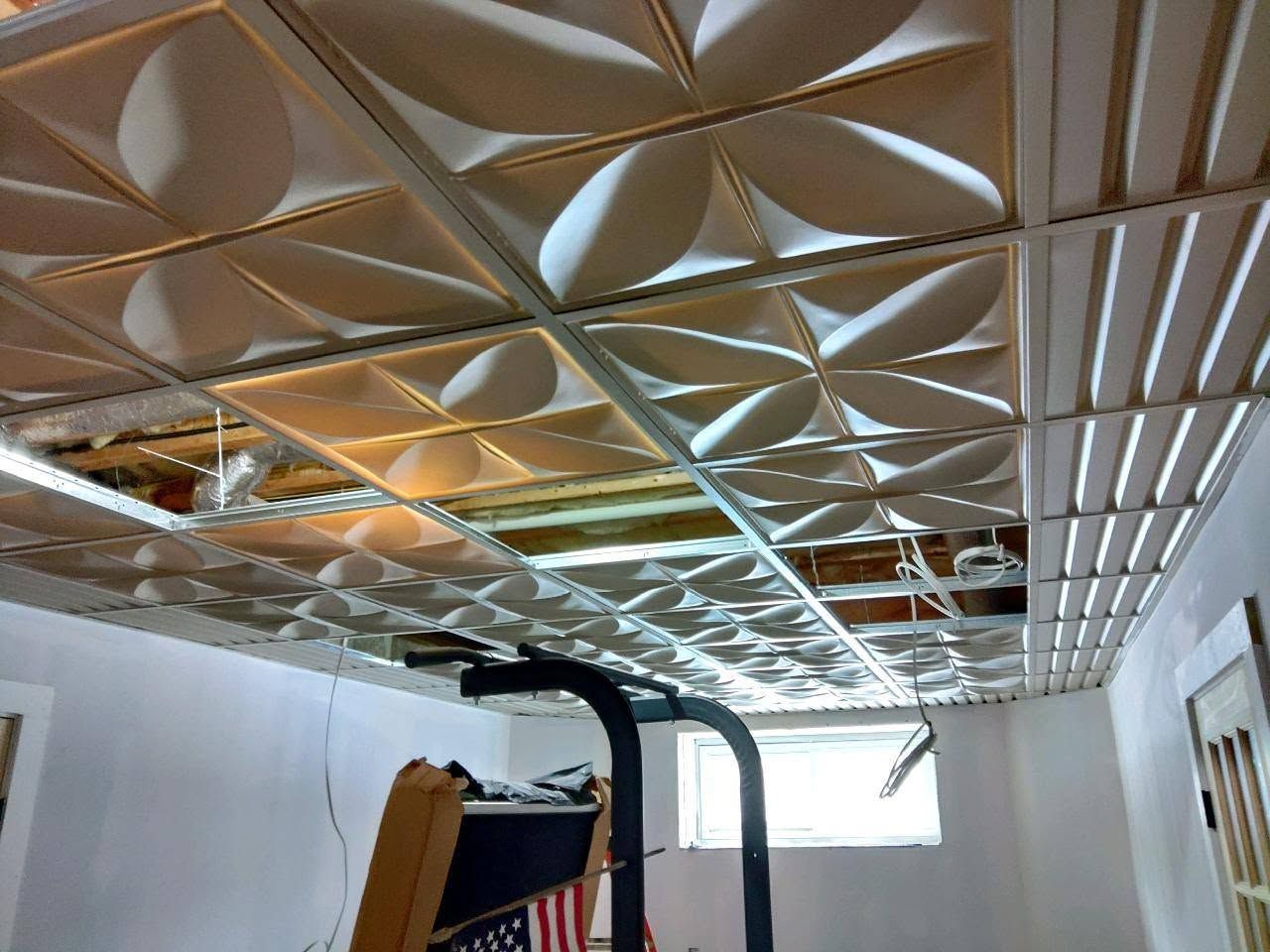 Damaged ceiling panels in an indoor room with exposed insulation and construction equipment below