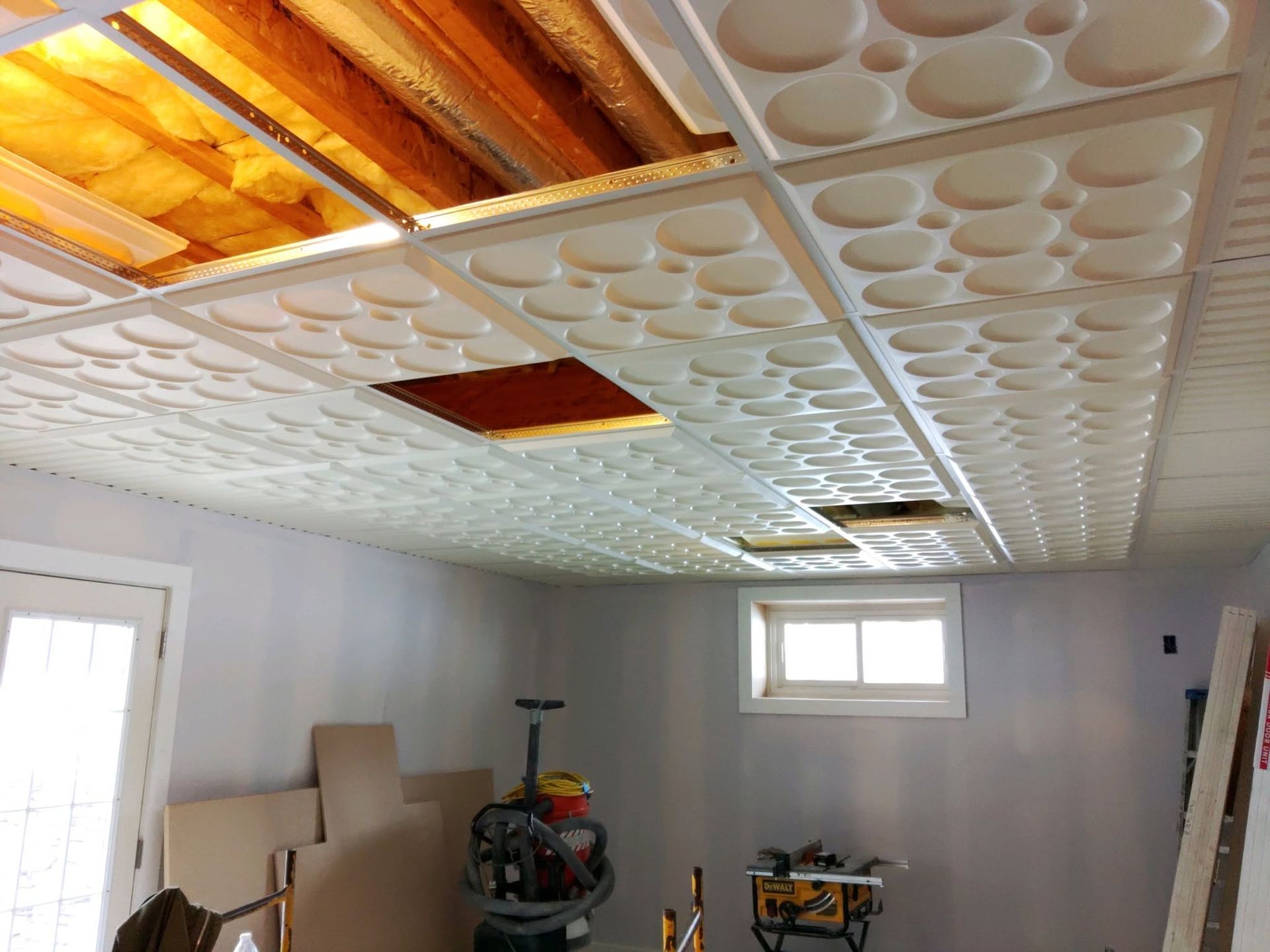 Partially finished room with patterned ceiling tiles, exposed wood, and construction tools inside.