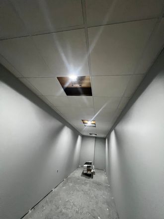 Narrow unfinished hallway with gray walls, exposed ceiling openings, and debris on the floor.