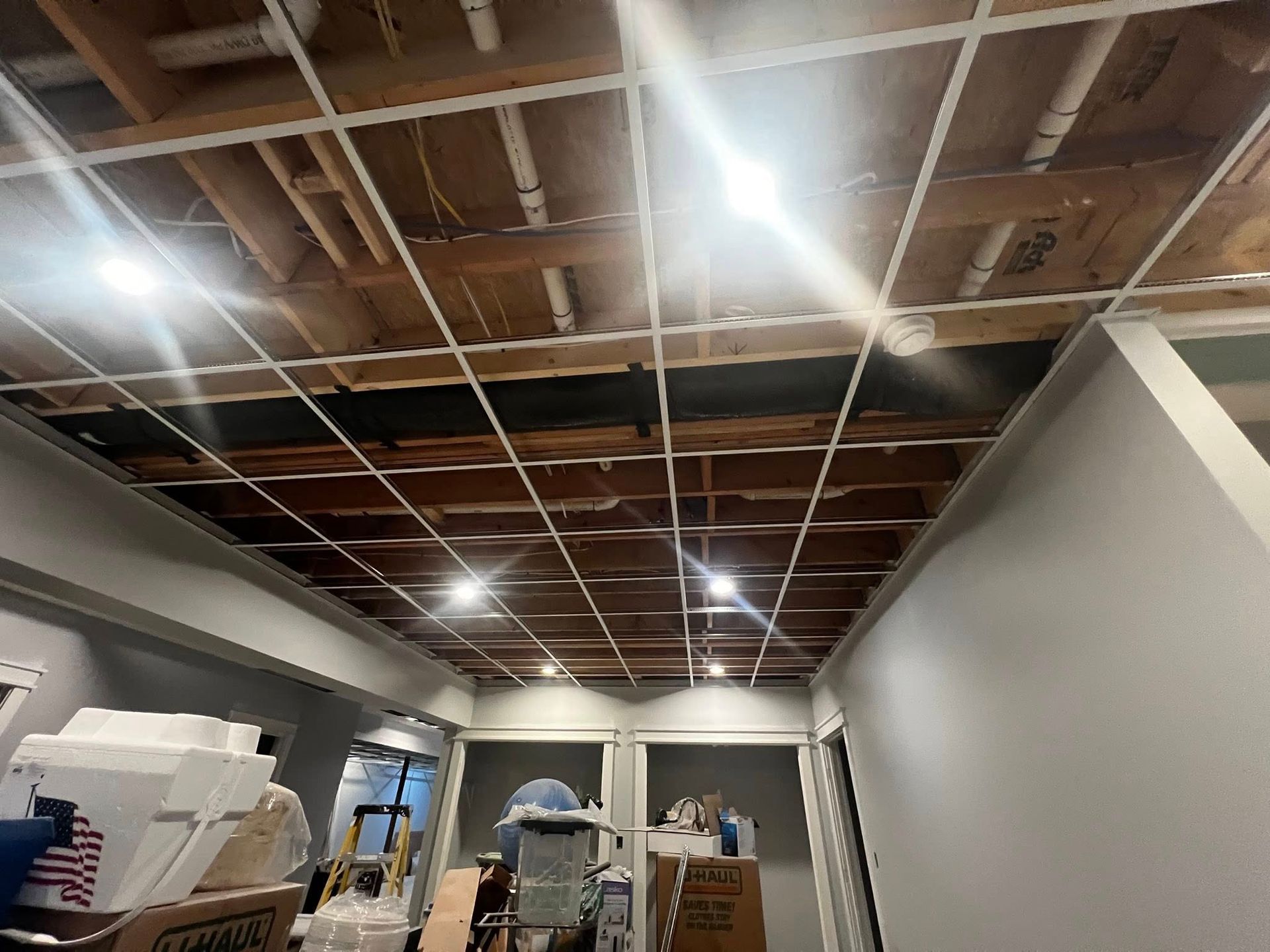 Renovated room with exposed ceiling beams, recessed lights, and stacks of boxes and materials on the floor