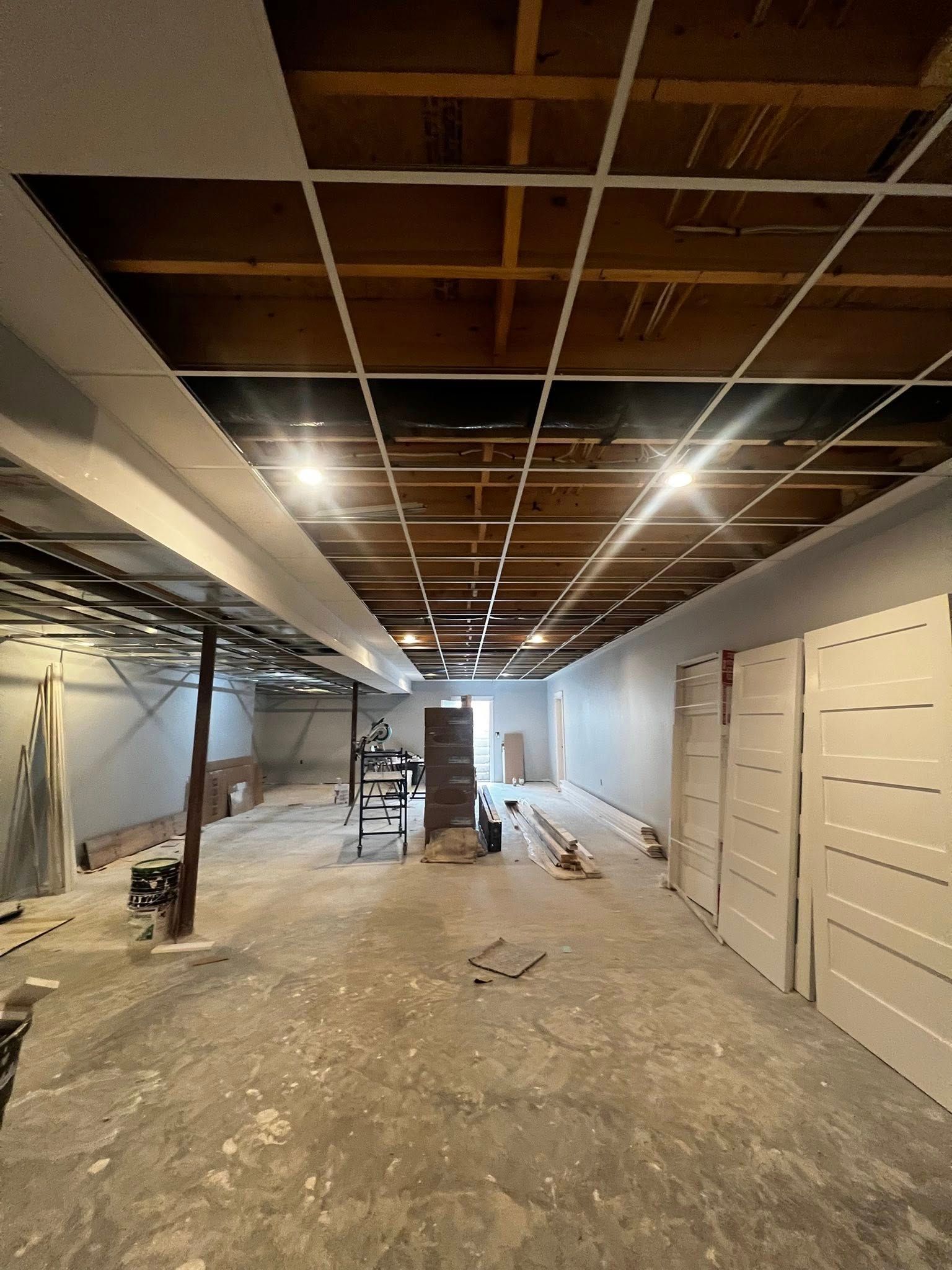Renovation site with exposed ceiling grid, debris-covered floor, and white walls under construction.