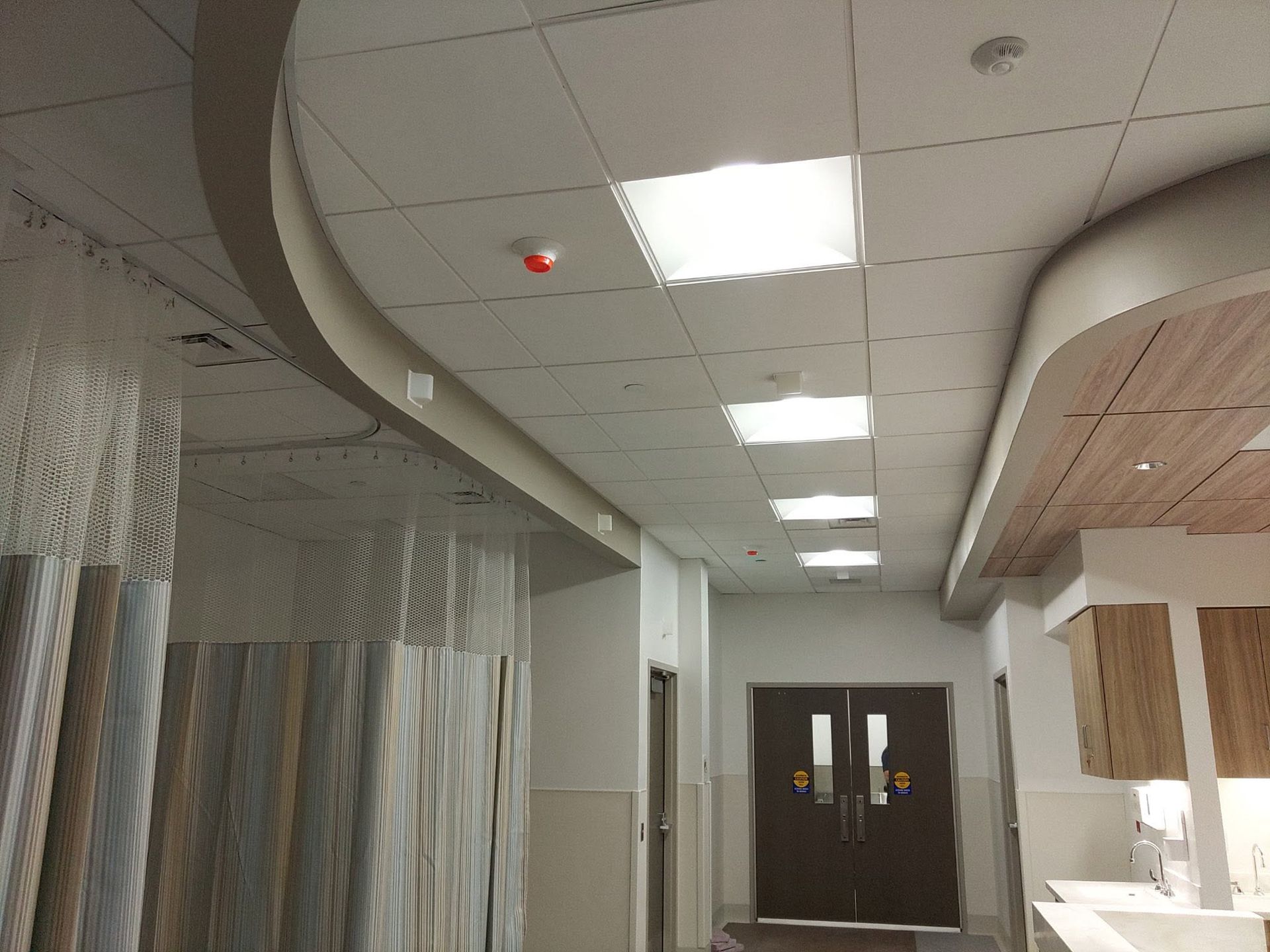 Empty hallway with ceiling lights, dark double doors, and patterned wall panels.