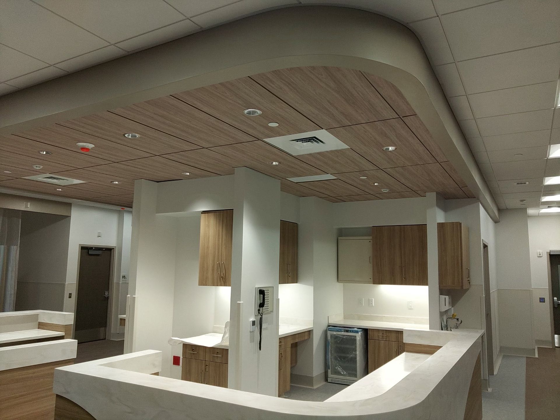 Modern kitchen showroom with wood cabinets, white counters, and a curved wood ceiling.