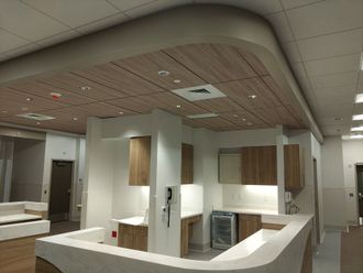 Modern office kitchenette with white counters, wood cabinets, and a curved wood ceiling panel