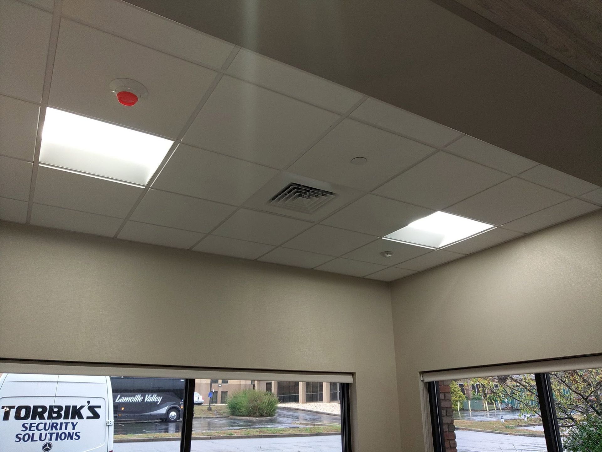 Office ceiling with fluorescent lights, air vent, and top of windows above a storefront sign.