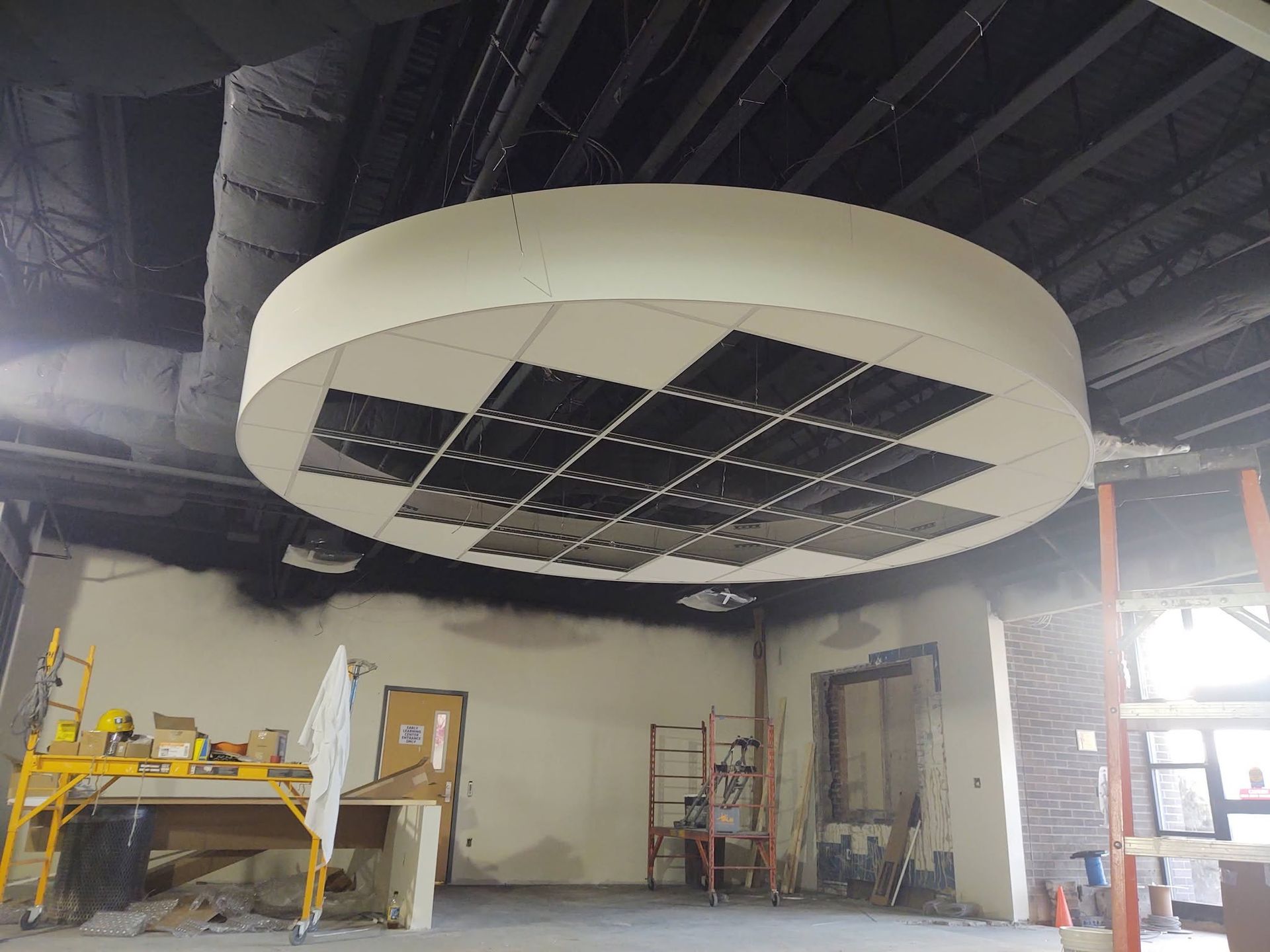 Large circular ceiling installation with dark solar-panel-like sections in an industrial warehouse interior