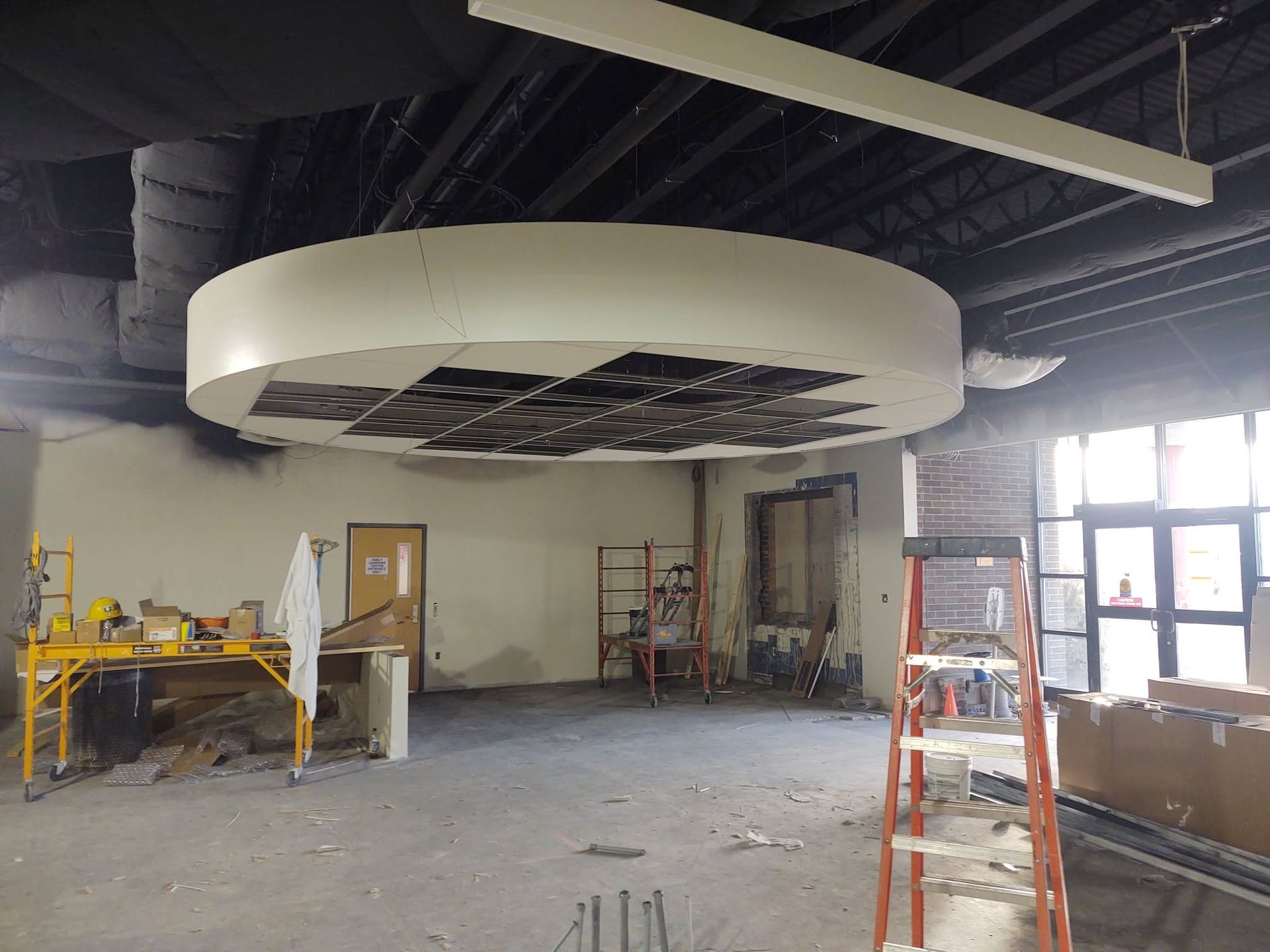 Unfinished room with a large circular ceiling feature, ladders, tools, and construction materials.