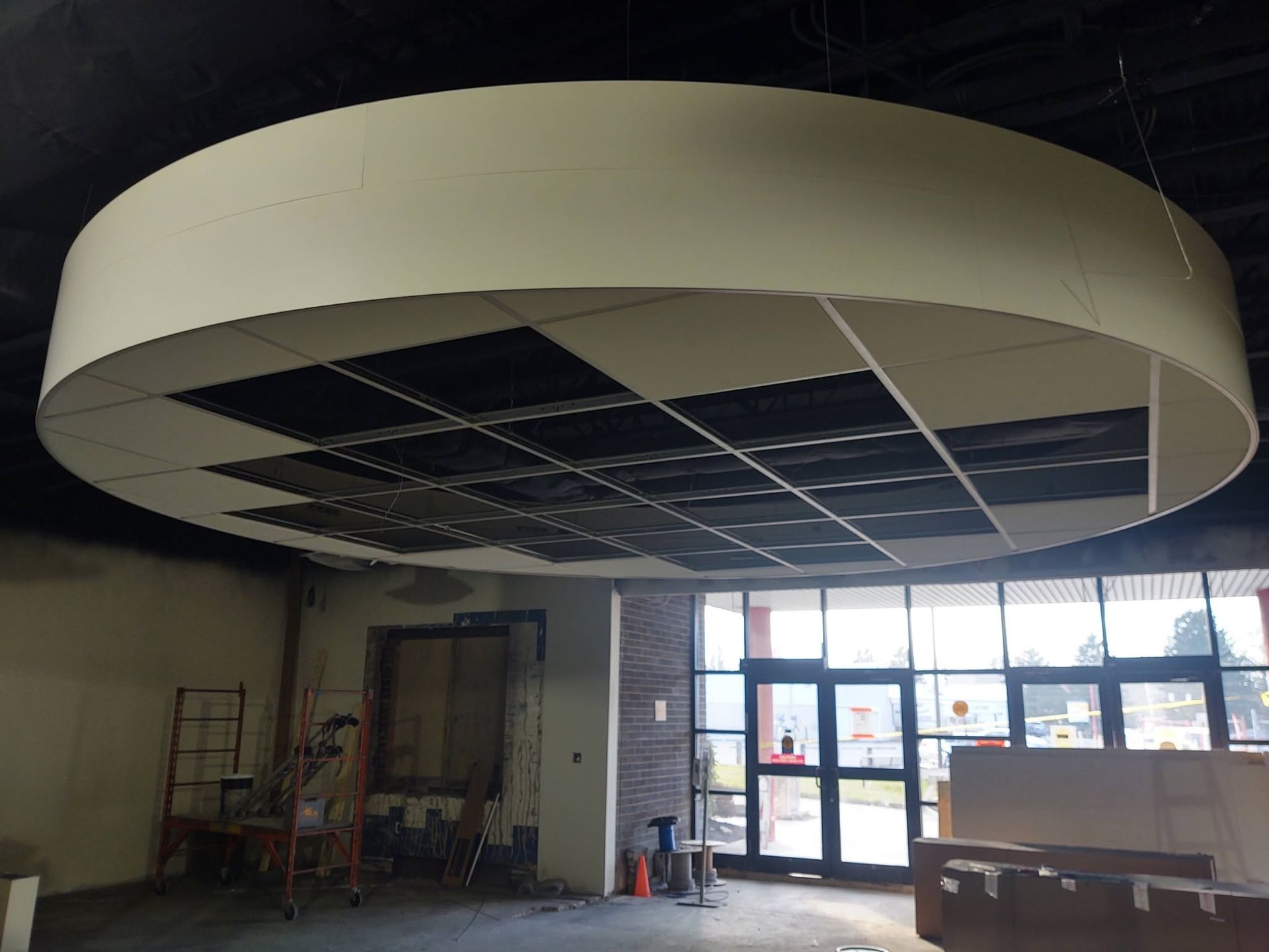 Large circular ceiling feature with a black grid in an unfinished room near glass doors.