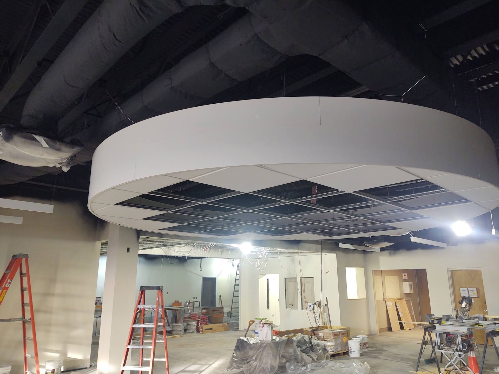 Construction site with large white circular ceiling feature and ladders in an unfinished room