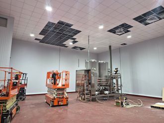 Empty warehouse interior with lifts, scaffolding, and damaged ceiling panels being repaired
