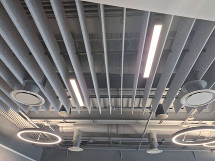 Ceiling with exposed gray beams, circular lights, and long fluorescent fixtures in an industrial interior