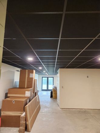 Empty office space with stacked cardboard boxes, drop ceiling, and glass doors at the far end.