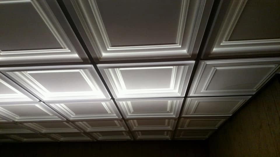 White coffered ceiling with recessed square panels and soft lighting in a dim room