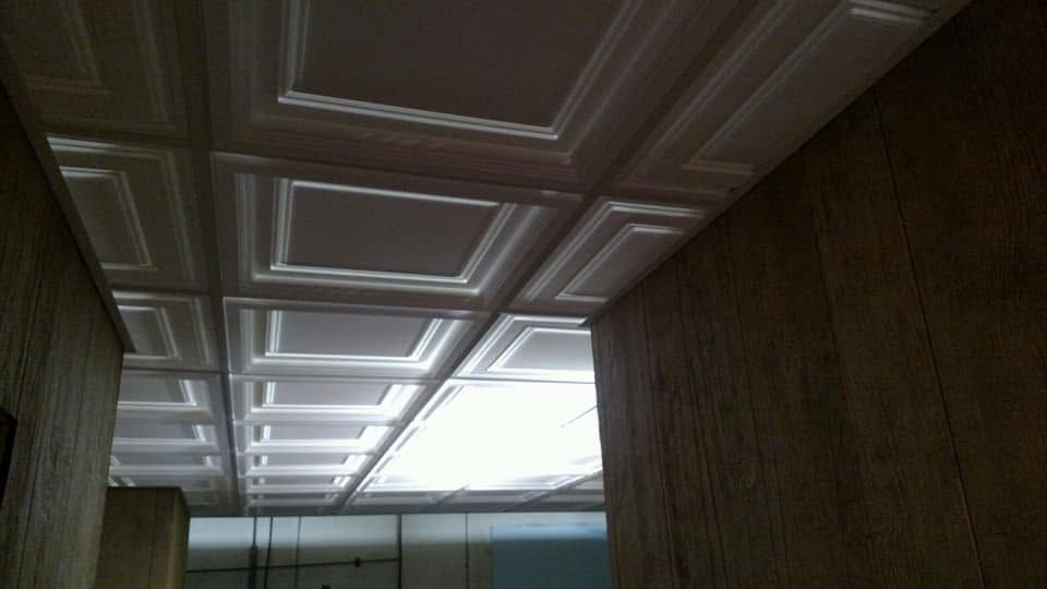 Ceiling with decorative square panels in a dim hallway, lit by bright skylight panels.