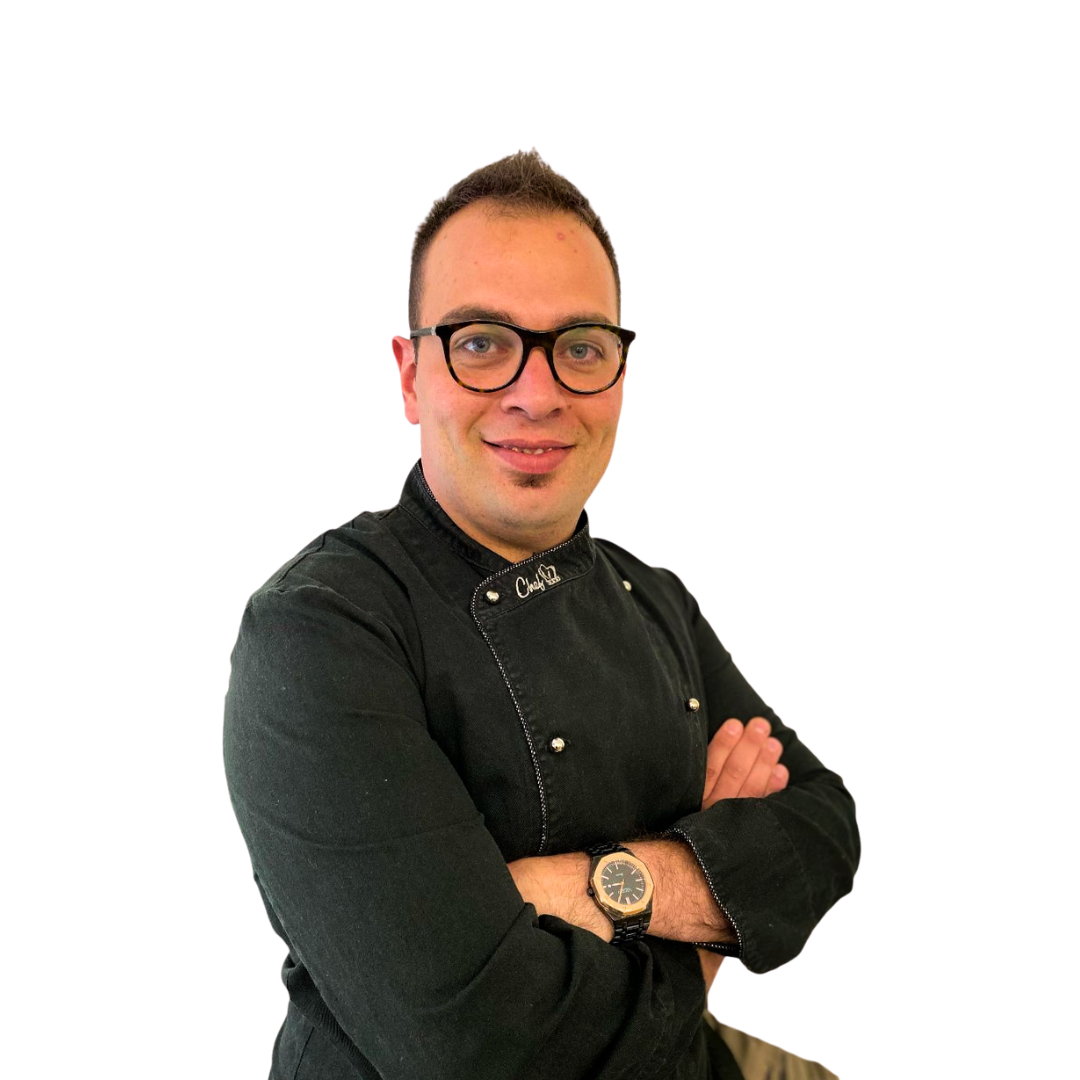 Mann in Kochuniform mit verschränkten Armen, Brille und Armbanduhr, lächelnd.