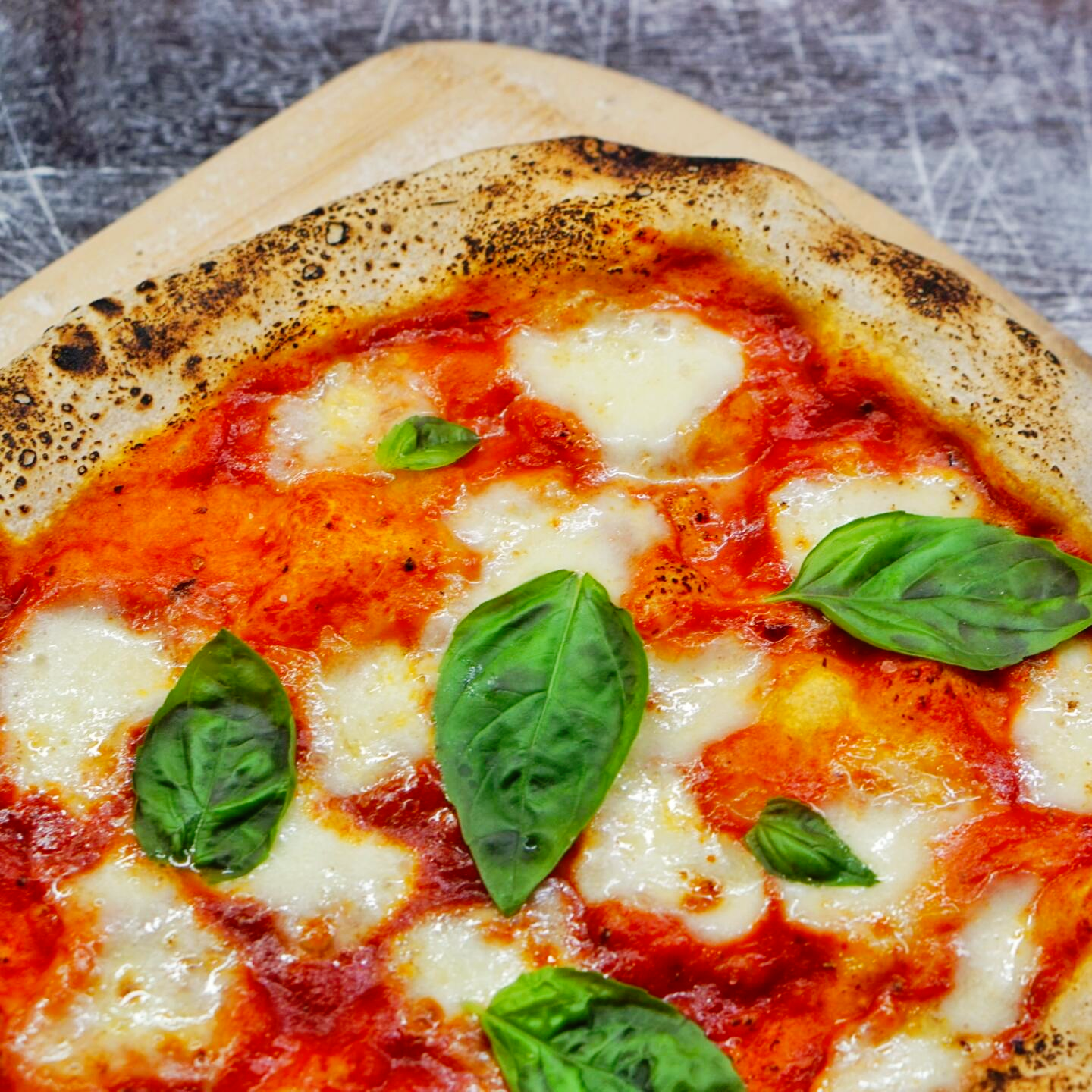 Pizza margherita with tomato sauce, mozzarella, and basil on a wooden board.