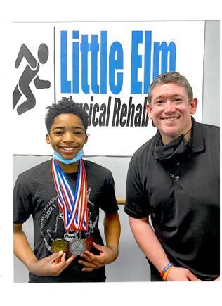 A man and a boy are posing for a picture in front of a little elm physical rehab sign.