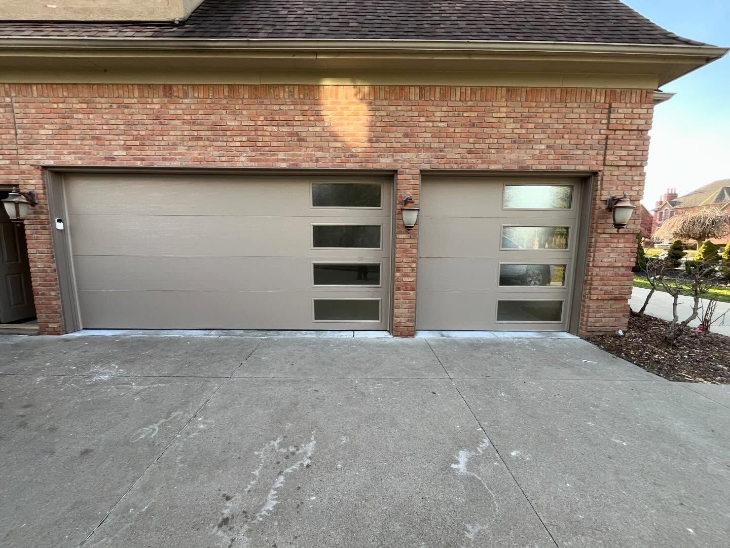 Two-car garage with tan doors and brick exterior, fronted by a concrete driveway