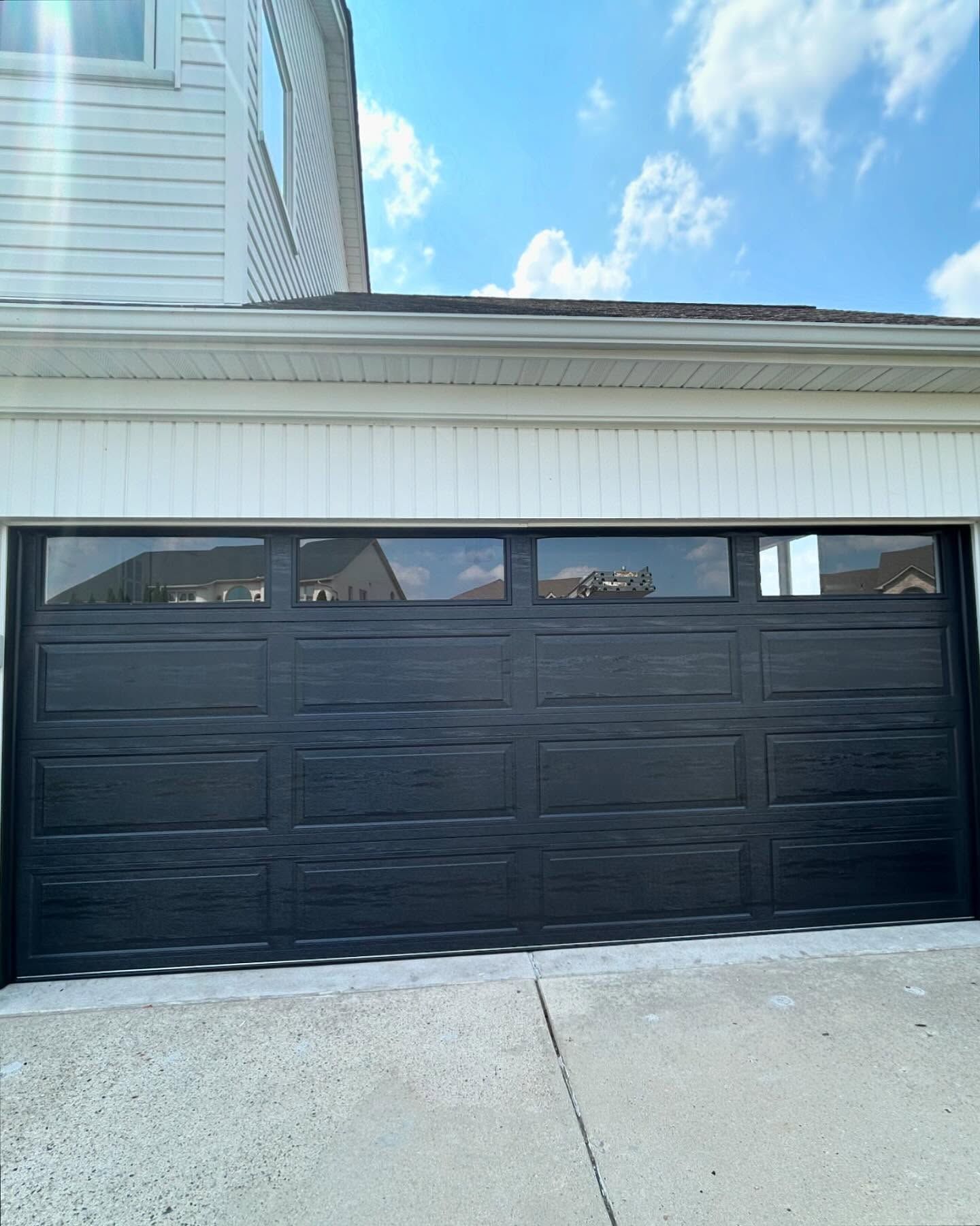 Black garage door with windows on a white house and driveway under a blue sky