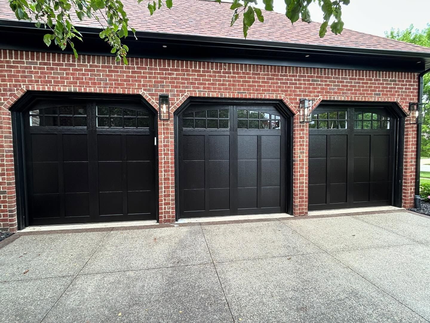 Three black garage doors on a red brick house with a concrete driveway