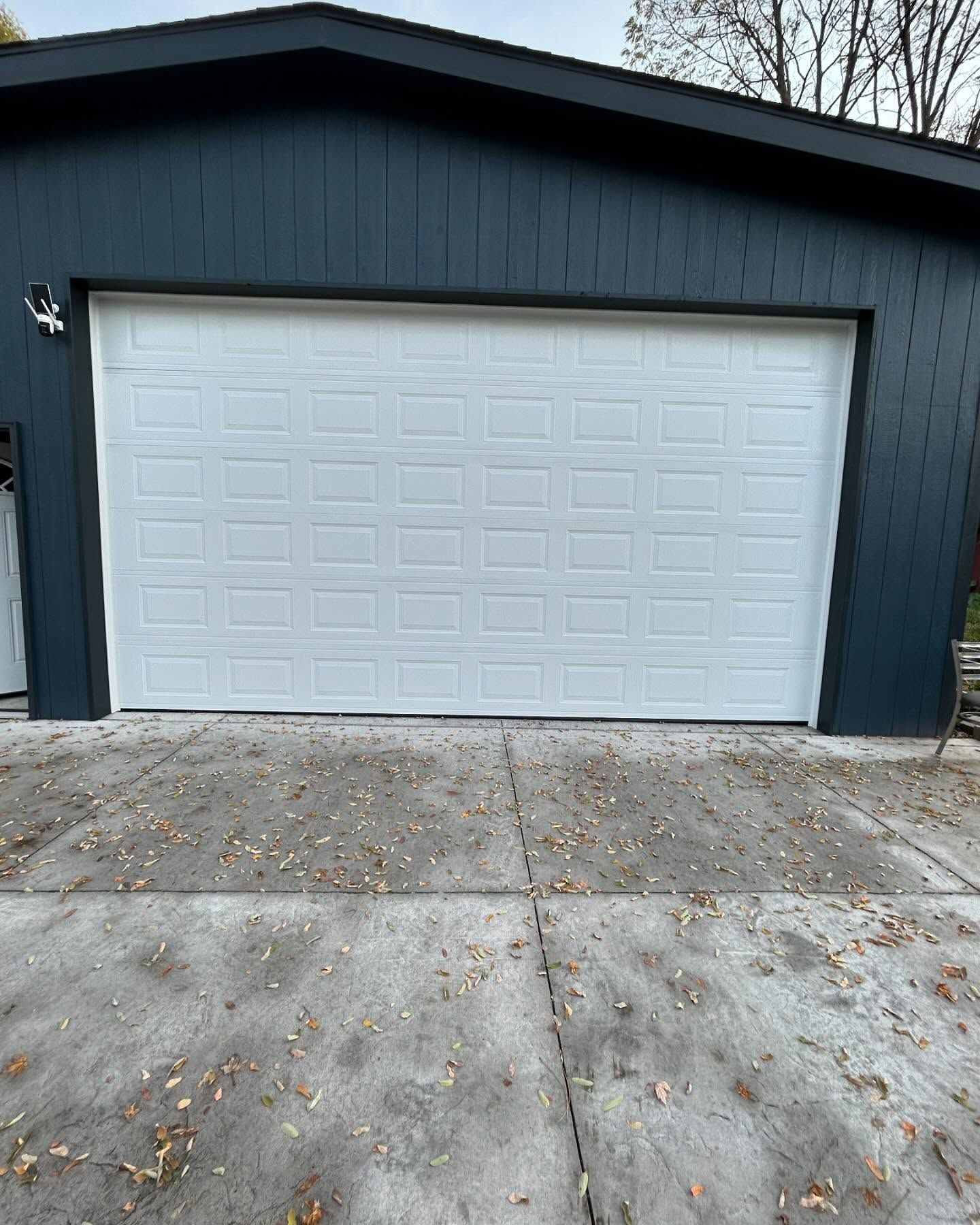 Dark blue garage with a white door and concrete driveway in front