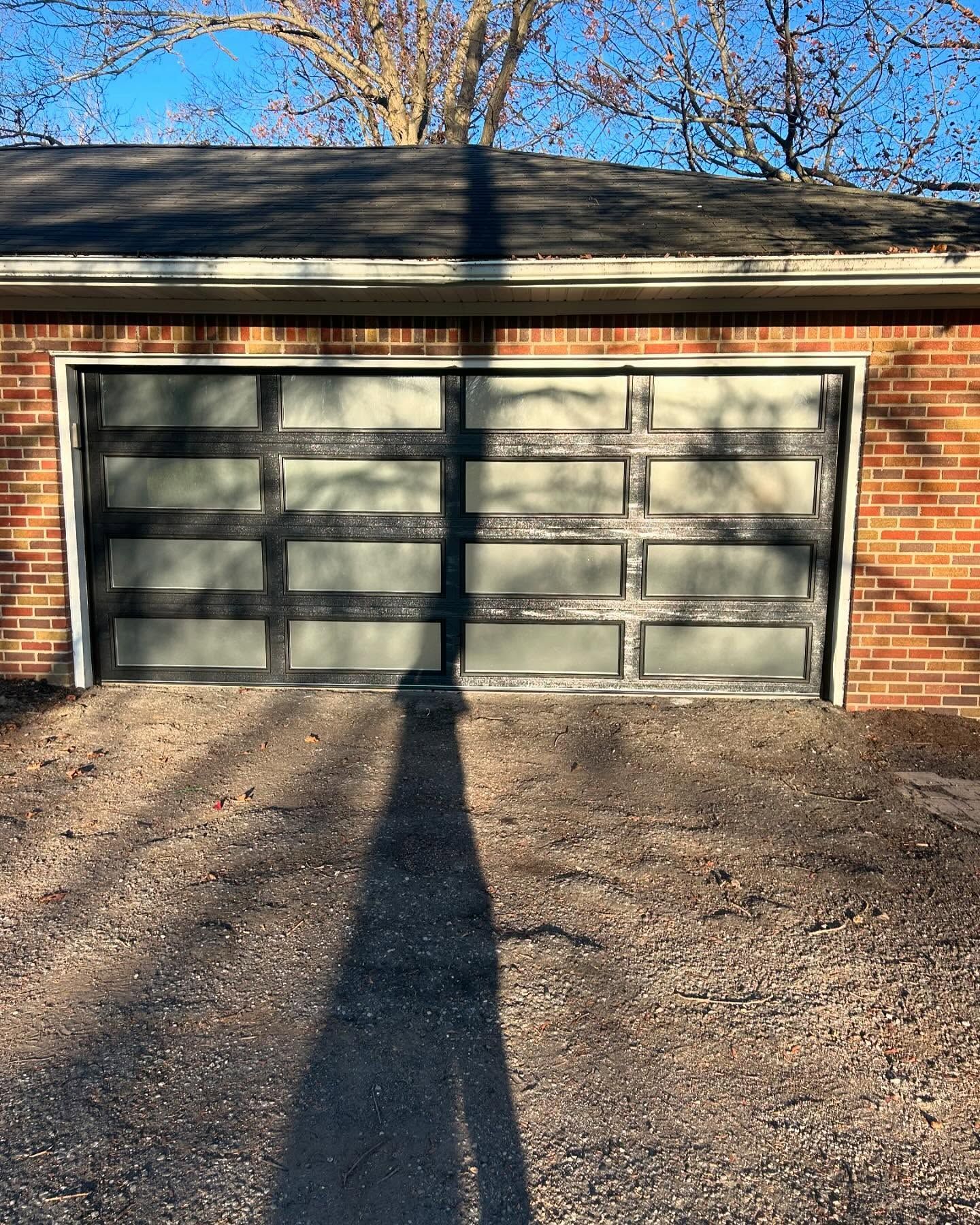 Brick garage with a gray double door and long shadows across the driveway in sunlight