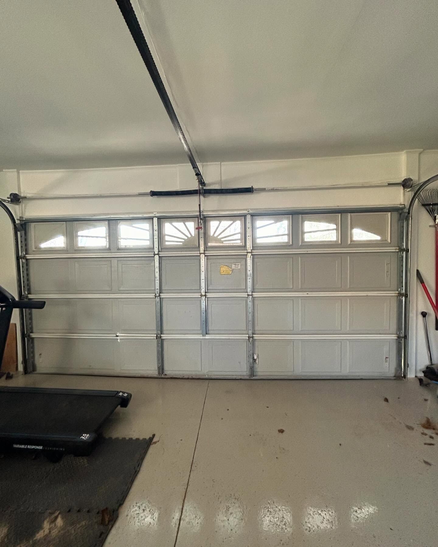 Garage interior with closed white paneled door and treadmill on the left