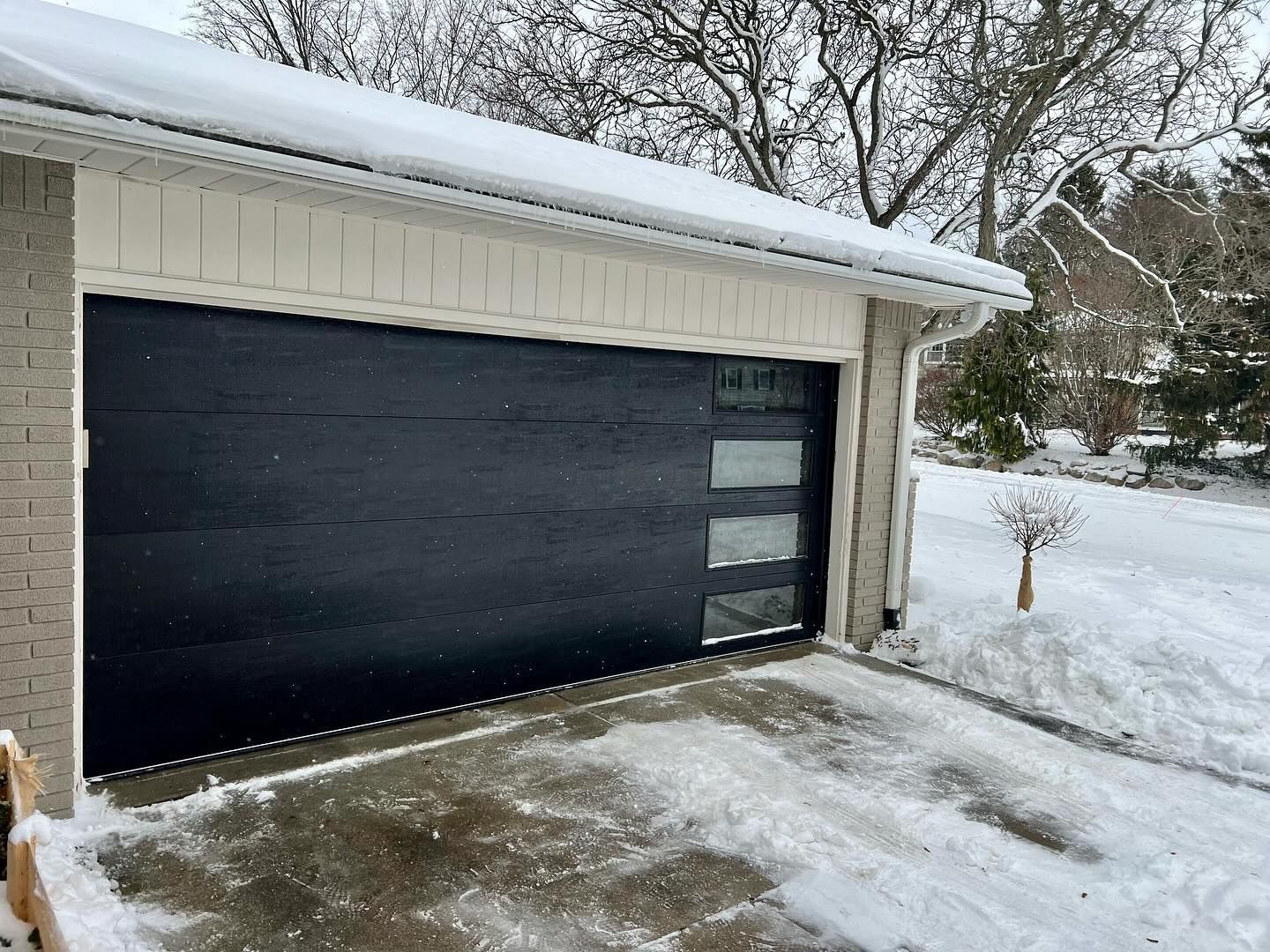 Snow-covered driveway in front of a dark garage door with frosted window panels.
