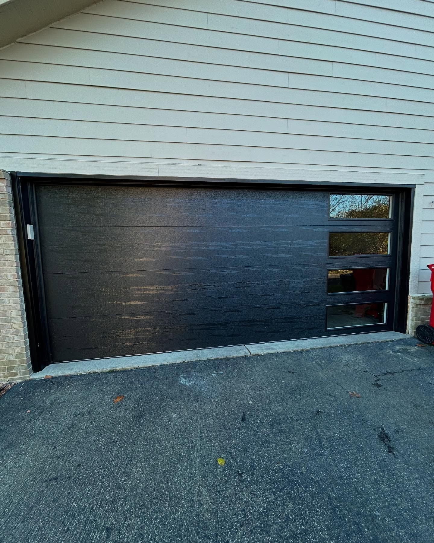 Black garage door on a beige house with a small window panel on the right.