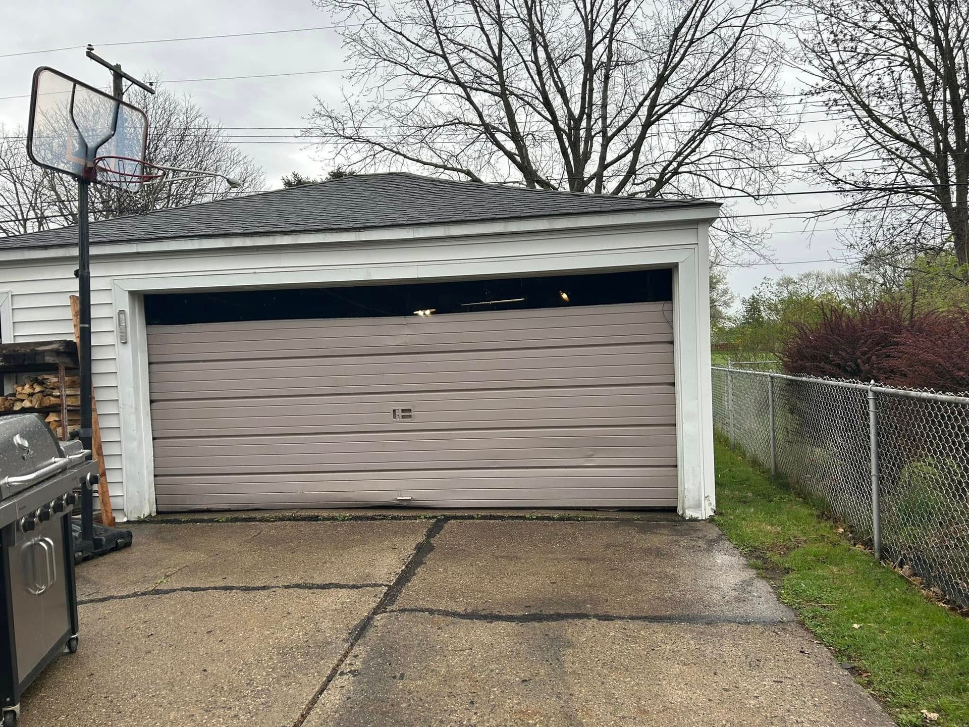 Detached garage with a closed beige door beside a driveway and fenced yard