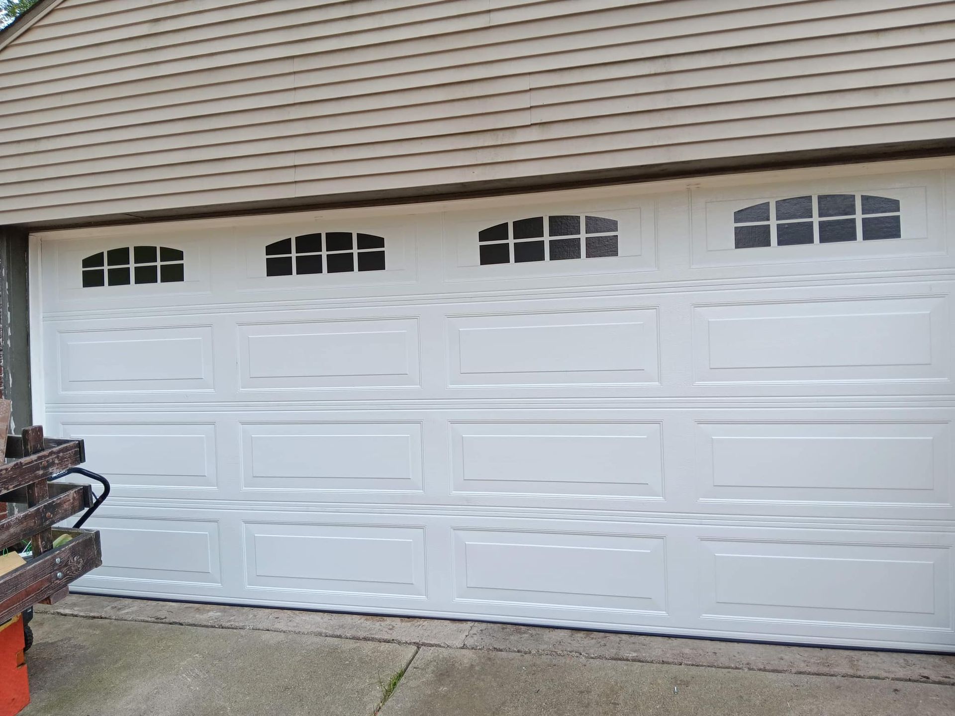 White two-car garage door with decorative windows on a beige house exterior