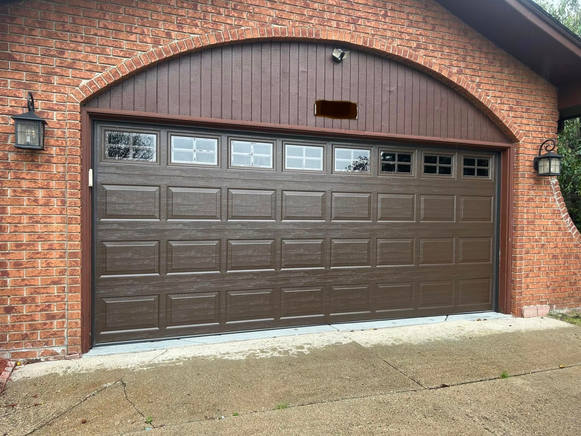 Brown garage door on a brick house with an arched wood-trimmed frame