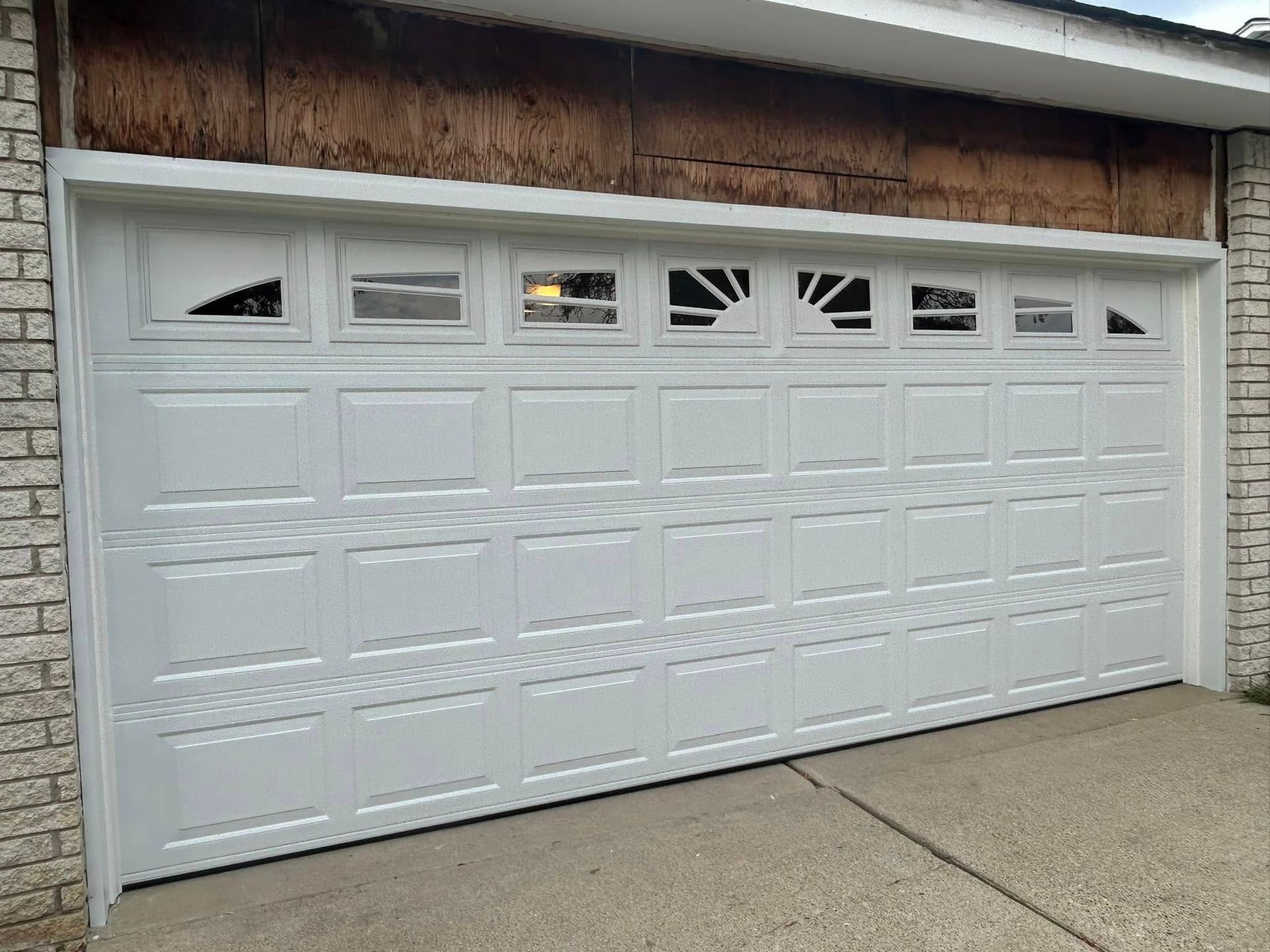 White paneled garage door with small windows under a wood-trimmed roof.