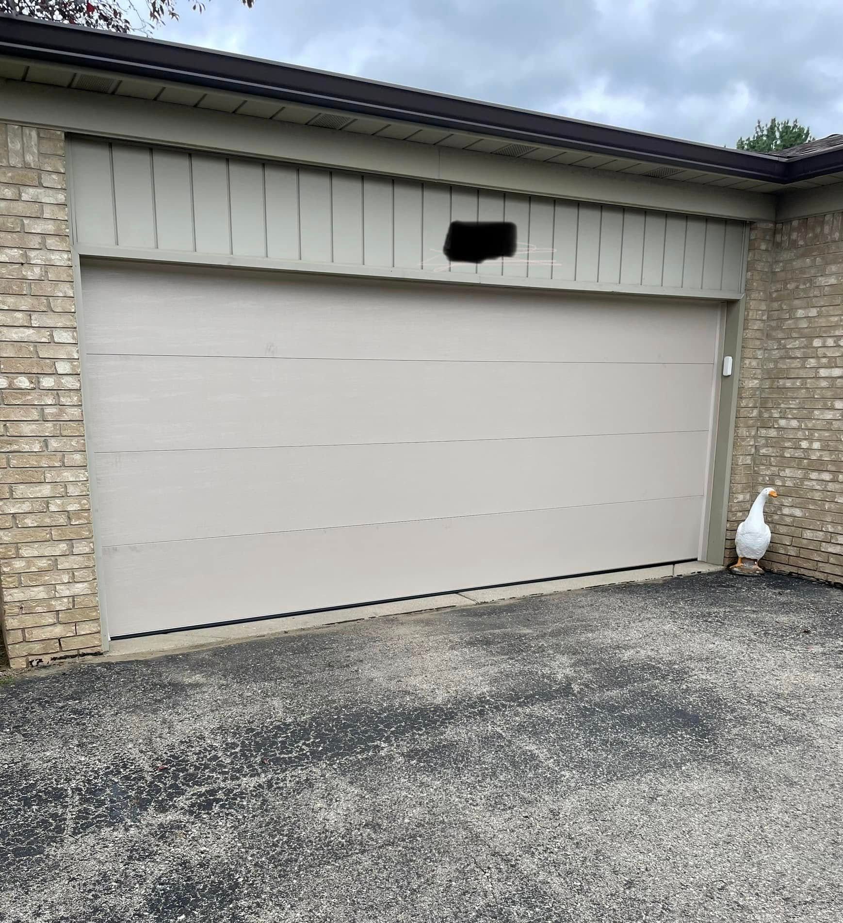 Closed beige garage door with stone walls and a white goose standing at the right side.