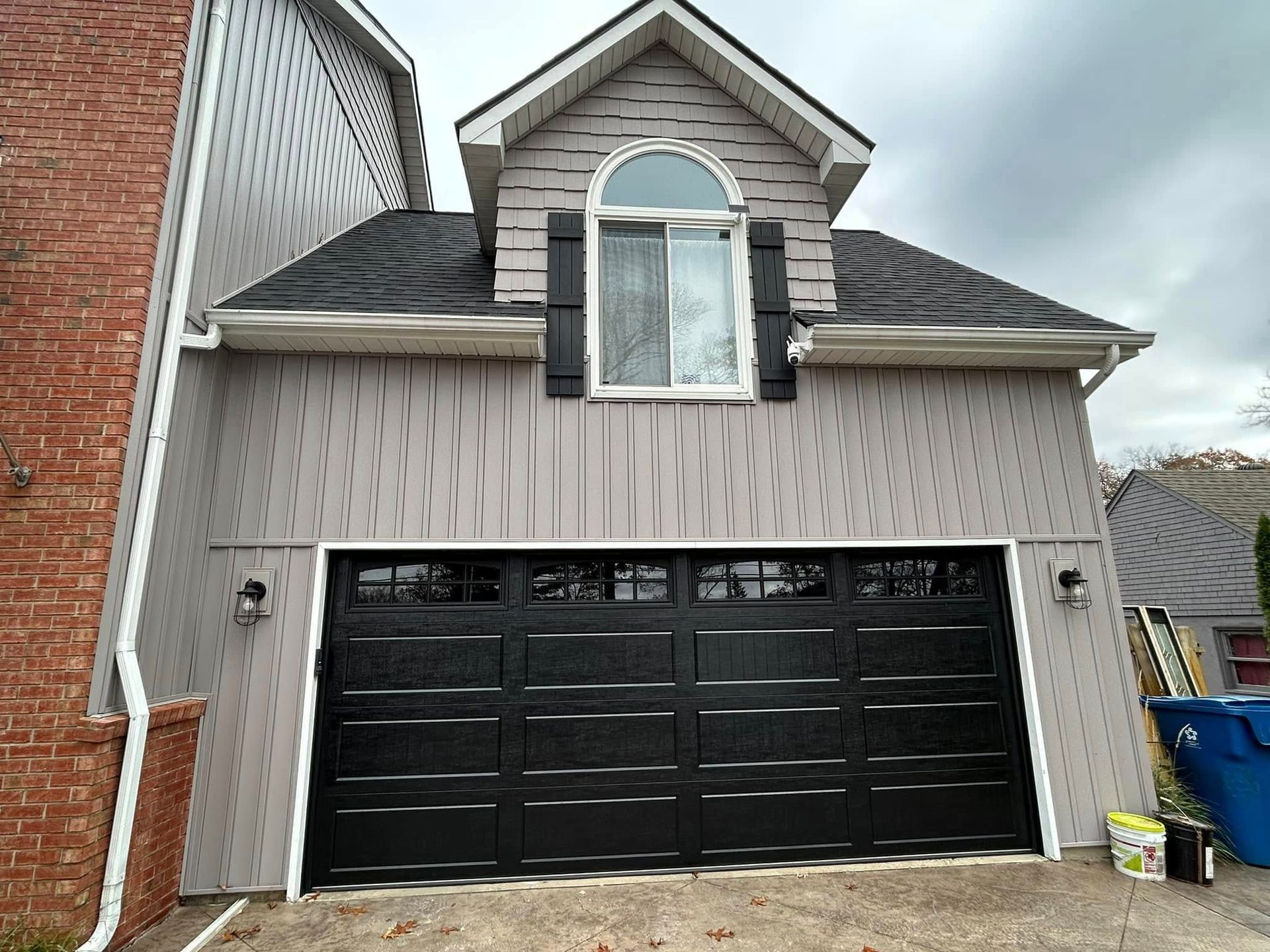 Two-car garage with black doors and a small dormer window above, on a beige house exterior