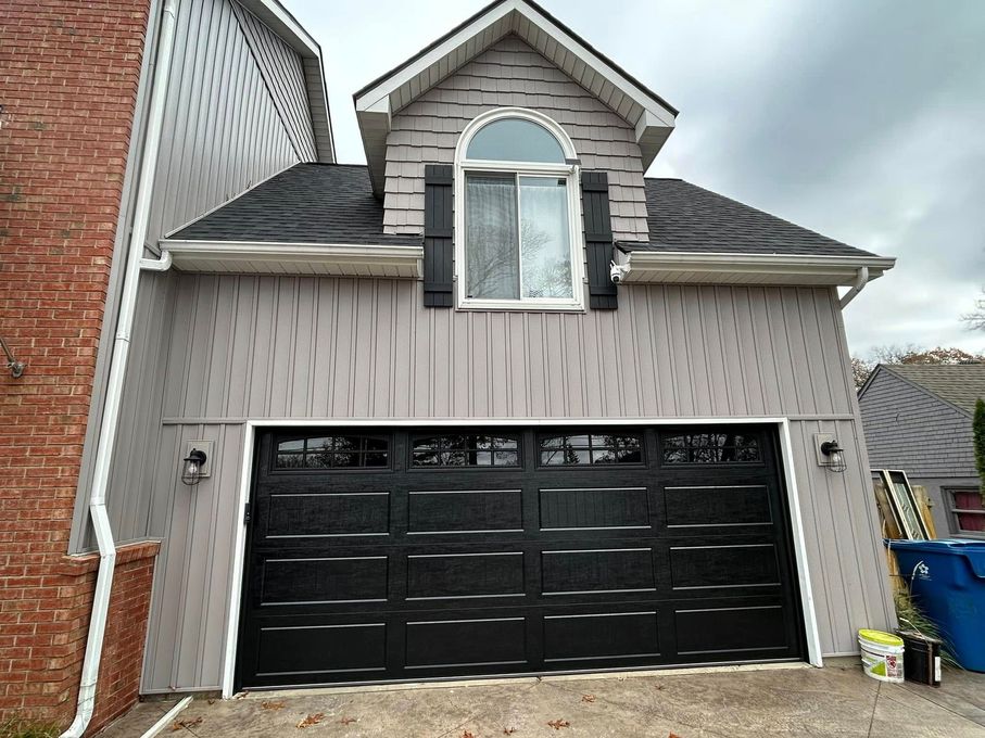 Two-car garage with black doors and a small dormer window above, on a beige house exterior