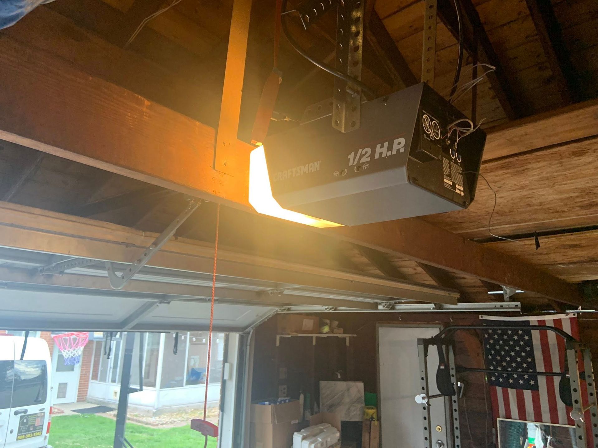 Garage ceiling with a suspended projector and a partially open door, lit by warm sunlight.