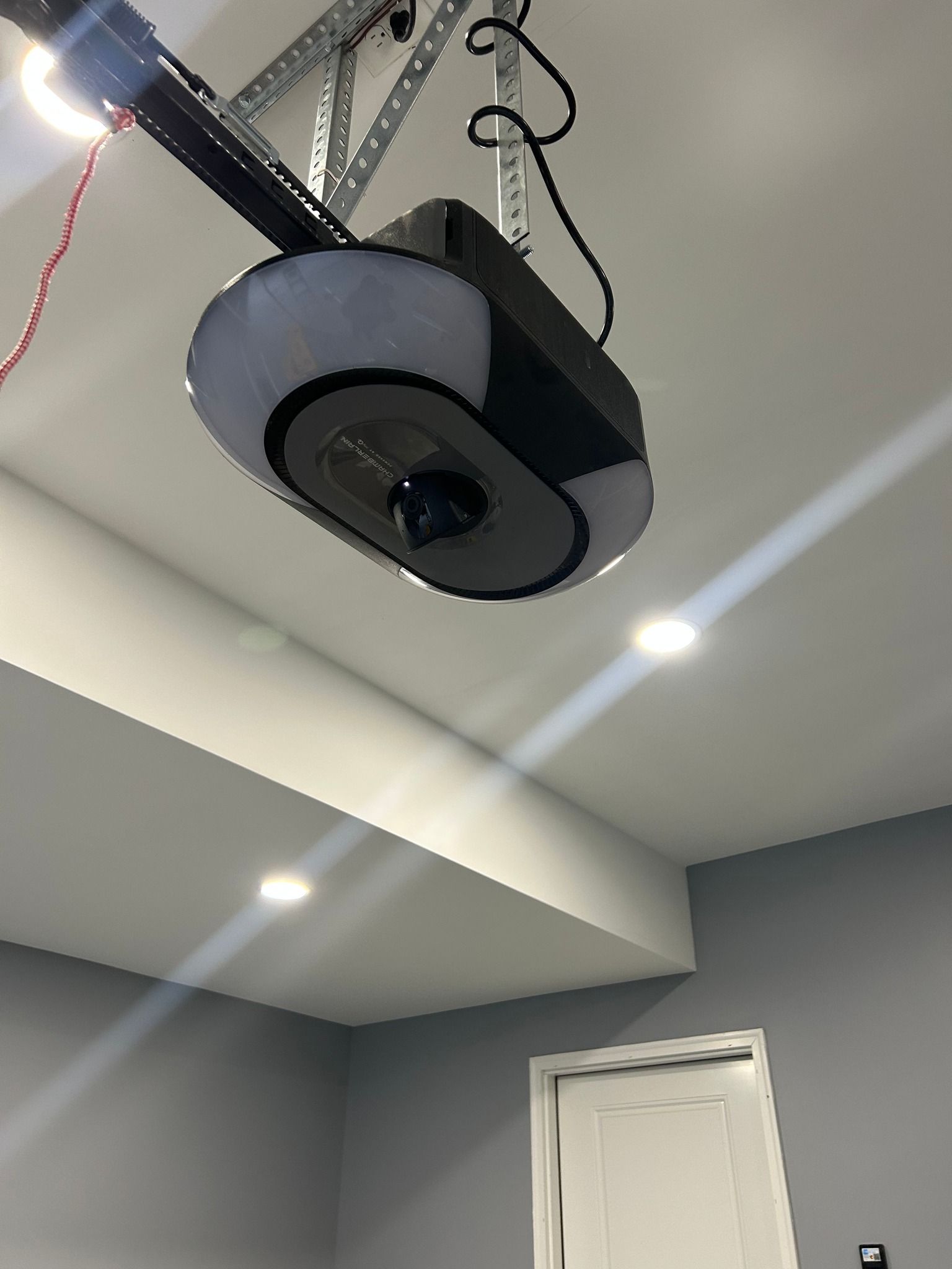 Ceiling-mounted projector in a gray room above a white door, with recessed lights overhead