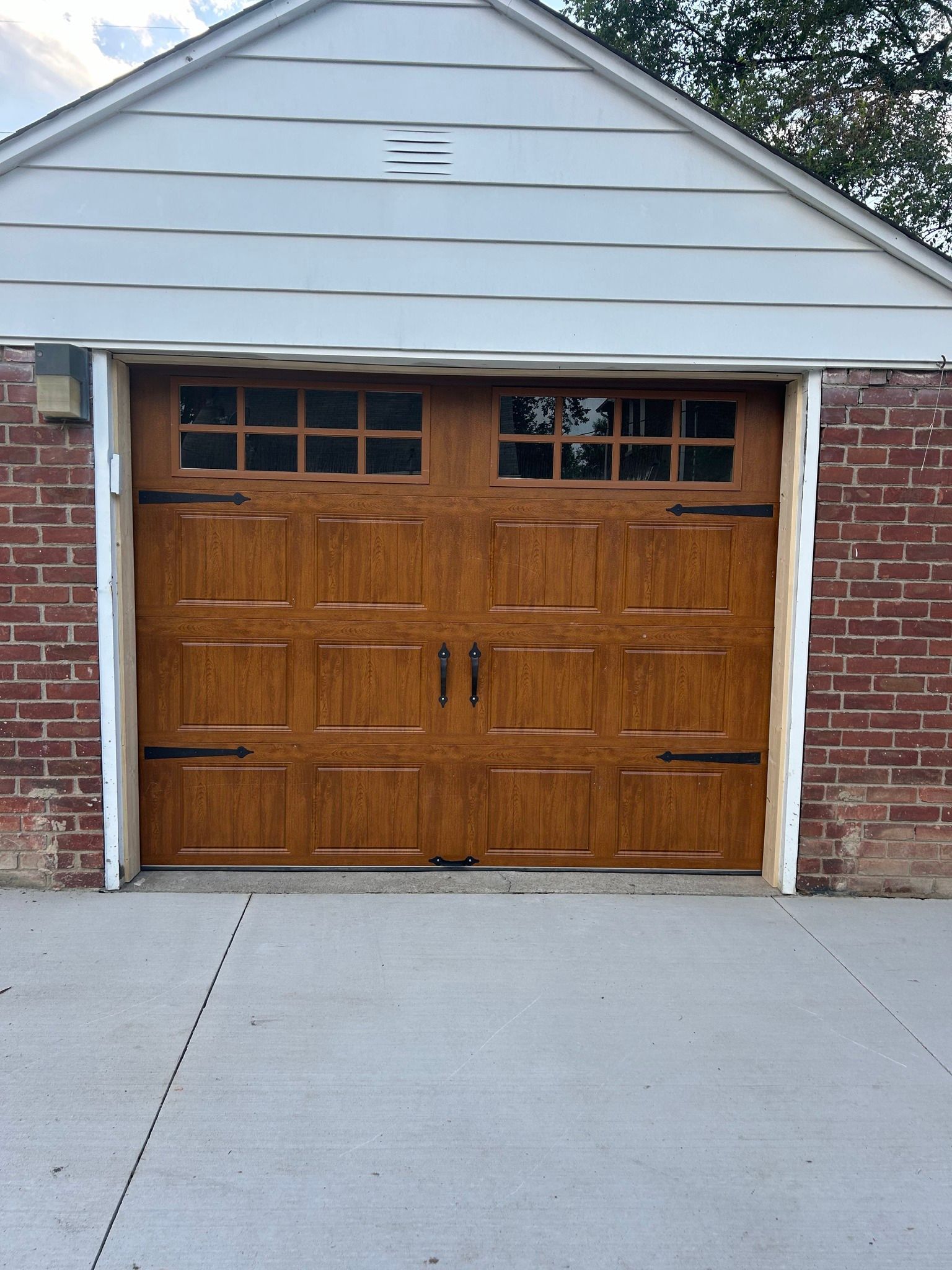 Wooden double garage doors beneath a light gray gable roof with brick siding and concrete driveway