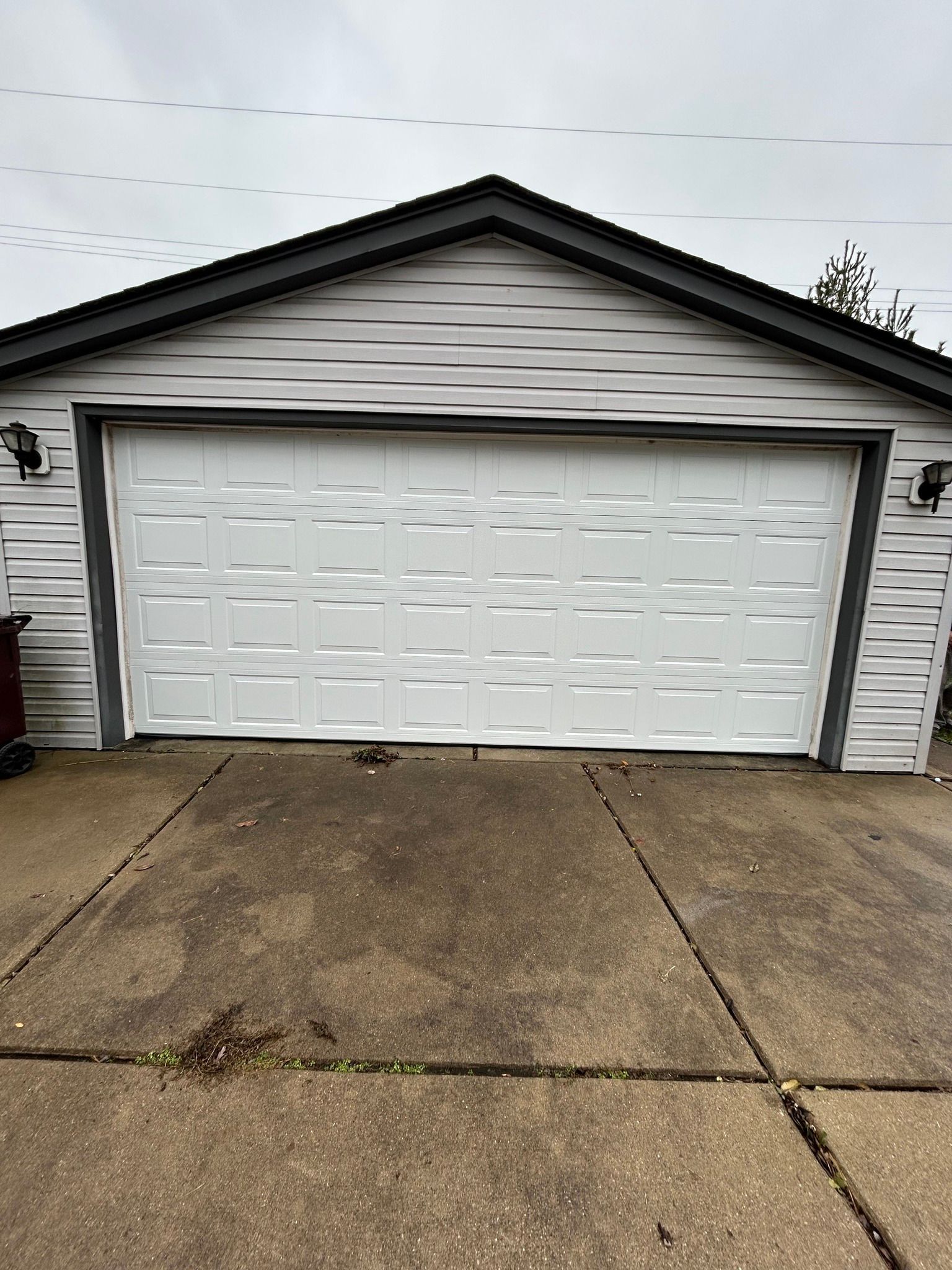 White double garage door on a gray house with a concrete driveway under an overcast sky