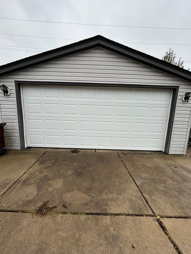 White double garage door on a gray house with a concrete driveway under an overcast sky