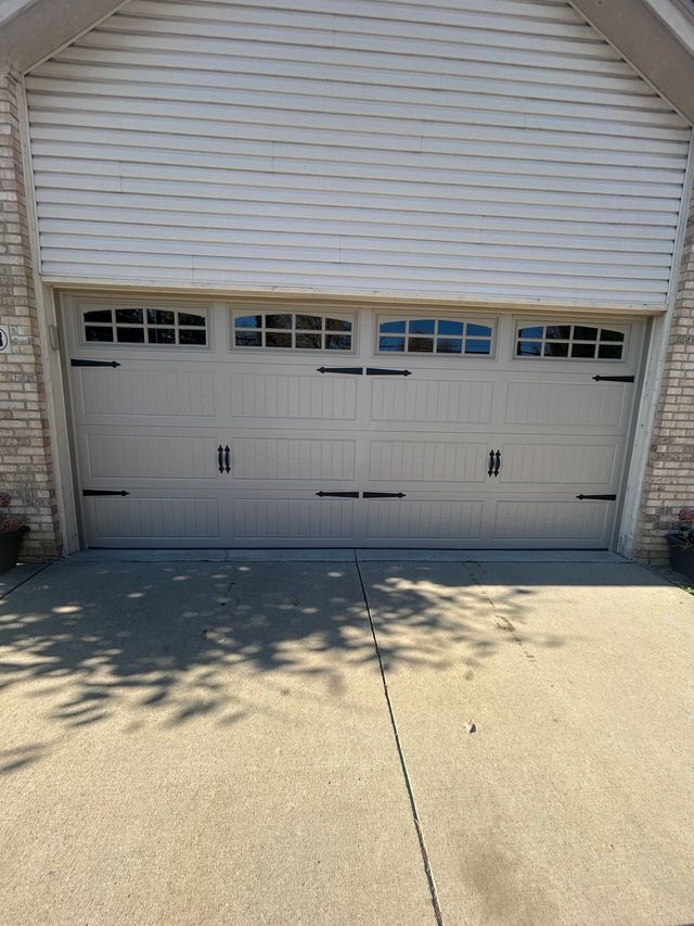 Closed light gray double garage door beneath beige siding, with a concrete driveway in front.