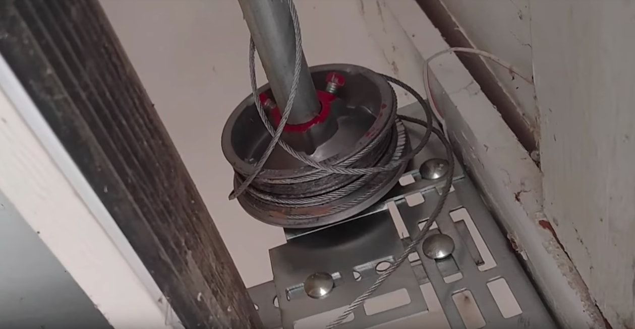 Coiled black hose or cable on a floor beside a wall and metal grate, with a red-tipped pipe above it
