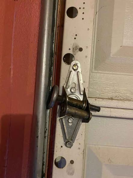 Close-up of a spring-loaded hinge latch on a white garage door frame.