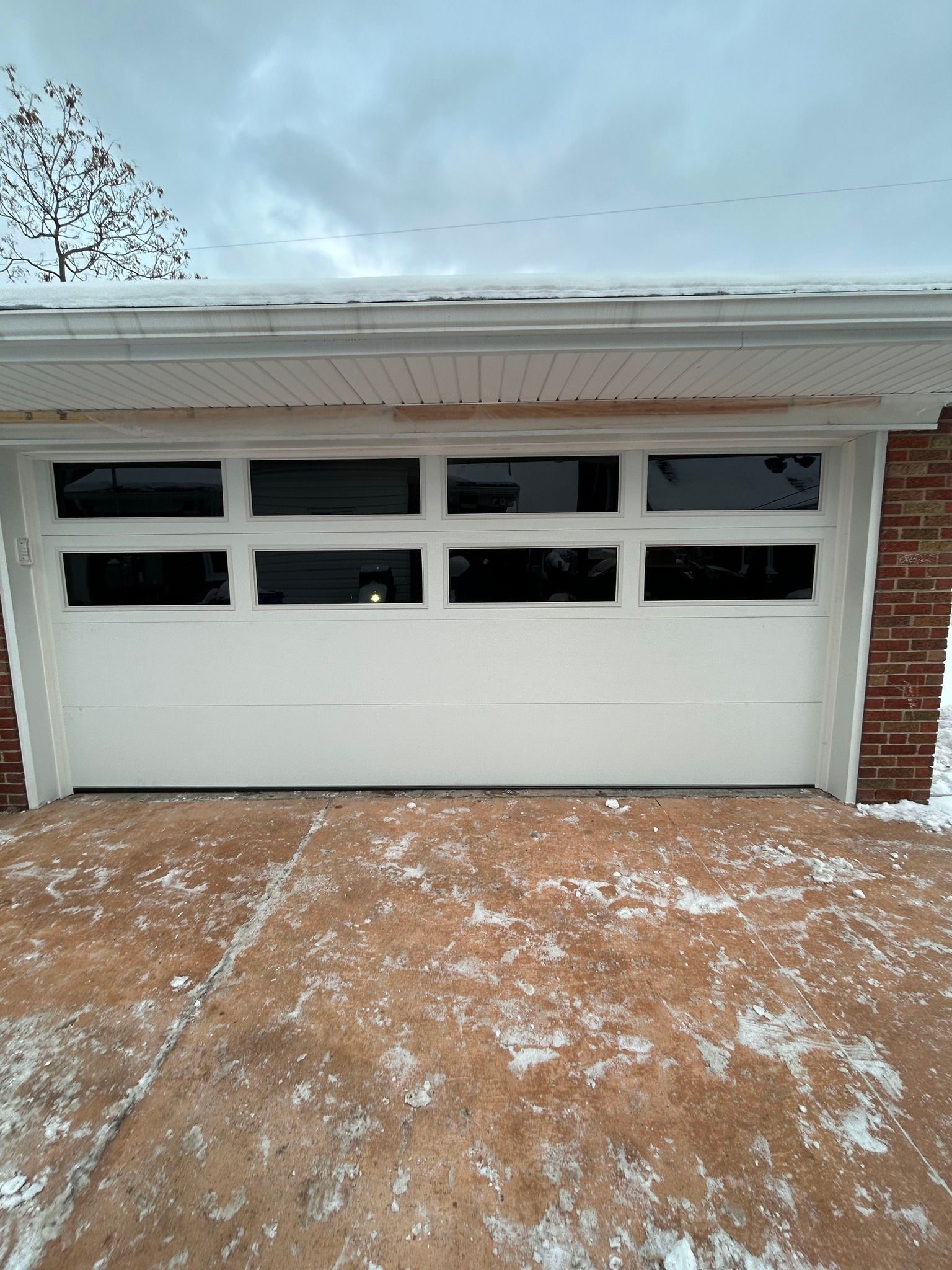 Snow-dusted driveway leading to a white garage door with three small windows