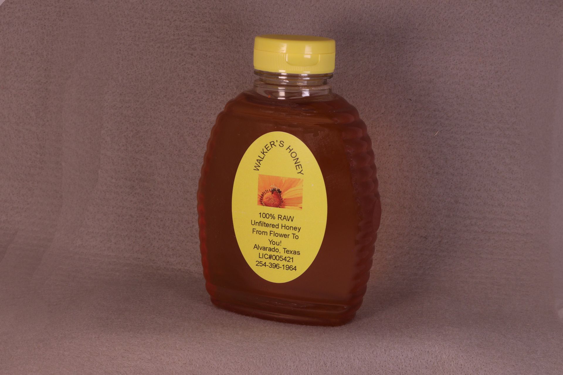 Plastic bottle of amber syrup with a yellow cap and oval label on a plain background