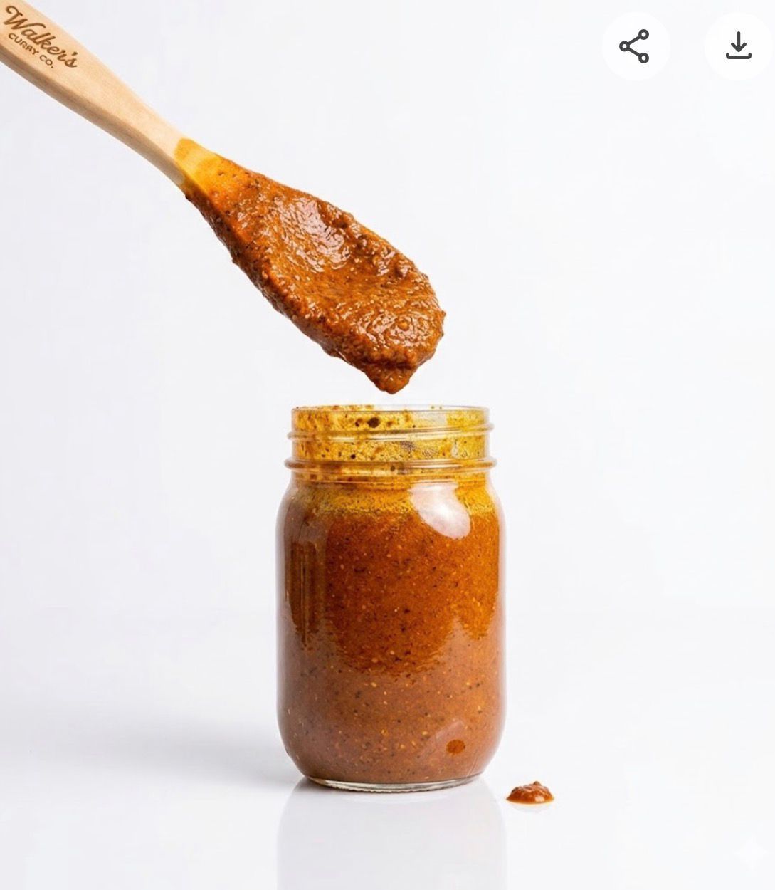 Wooden spoon lifting orange-brown sauce from a glass jar on a white background